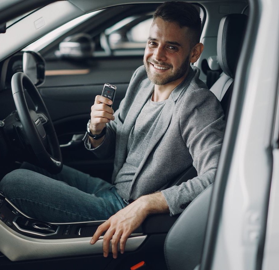 Besišypsantis vyras sėdi naujame automobilyje ir laiko raktelius